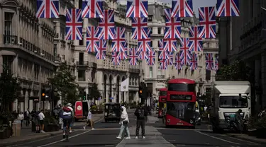 Orang-orang melintasi distrik perbelanjaan Regent Street dengan bendera Union tergantung menandai Platinum Jubilee untuk 70 tahun kepemimpinan Ratu Elizabeth II, di London, Rabu (18/5/2022). Tingkat inflasi Inggris naik ke level tertinggi dalam 40 tahun pada bulan April karena invasi Rusia ke Ukraina memicu kenaikan lebih lanjut dalam harga makanan dan bahan bakar. (AP Photo/Matt Dunham)