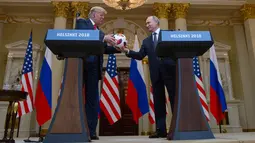 Presiden Rusia Vladimir Putin memberikan bola ke Presiden AS, Donald Trump pada konferensi pers bersama di Helsinki, Finlandia, Senin (16/7). Bola itu sebagai penghormatan karena AS akan menjadi tuan rumah Piala Dunia 2026. (AP/Pablo Martinez Monsivais)