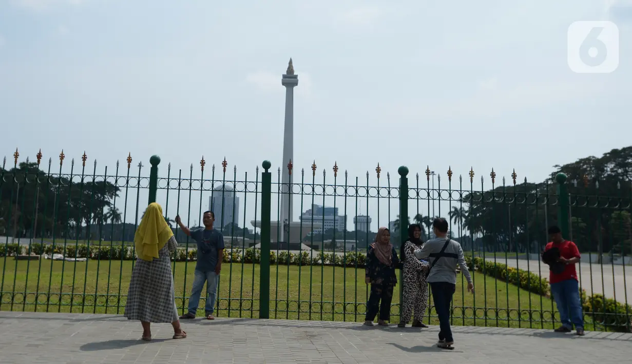 Warga berdiri di depan pagar Monumen Nasional (Monas), Jakarta, Sabtu (15/5/2021). Warga kecewa lantaran tempat wisata tersebut ditutup, padahal mereka datang untuk menikmati libur Idul Fitri 1442 Hijriah. (merdeka.com/Imam Buhori)
