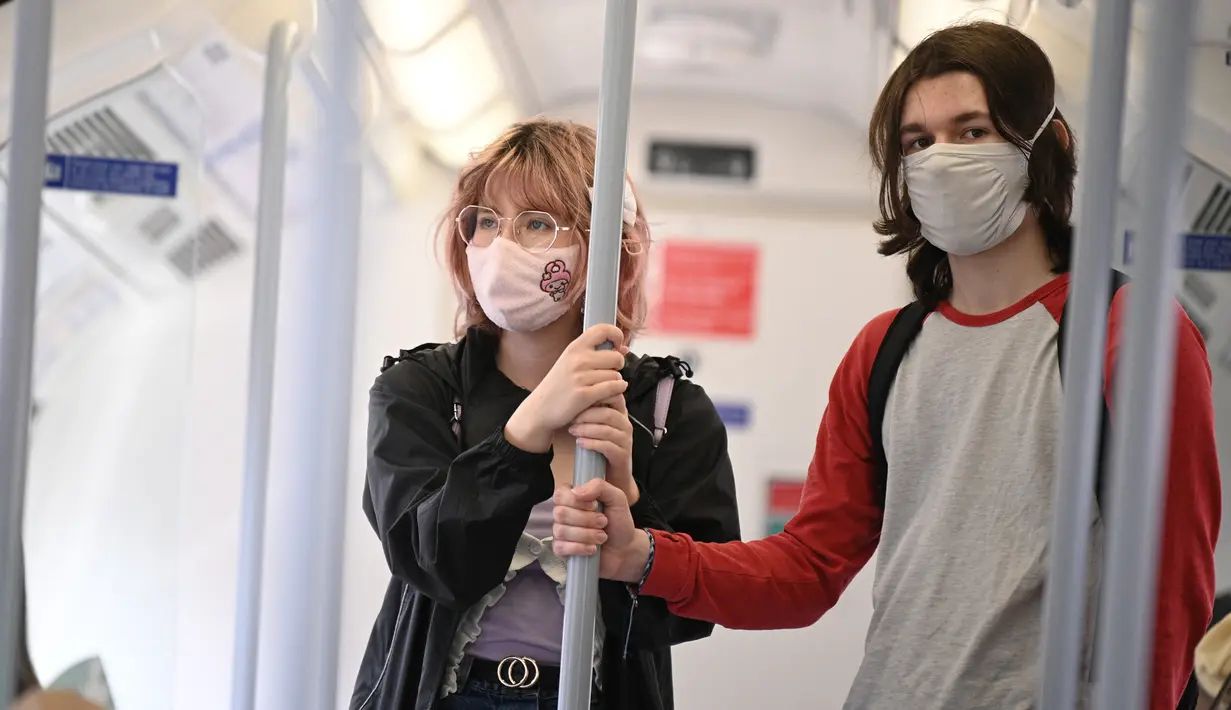 Para penumpang yang mengenakan masker menaiki kereta bawah tanah di pusat kota London, Senin (5/7/2021). PM Inggris Boris Johnson berencana mencabut sebagian besar pembatasan wilayah selama pandemi Covid-19, termasuk penggunaan masker dan jaga jarak mulai 19 Juli. (DANIEL LEAL-OLIVAS/AFP)