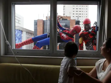 Petugas pembersih kaca menggunakan kostum Spiderman dan Iron Man menghibur pasien anak yang dirawat di RS Infantil Sabara, Sao Paulo, Senin (10/10). Aksi ini bagian dari perayaan Hari Anak Brasil yang diperingati tiap 12 Oktober. (REUTERS/Paulo Whitaker)