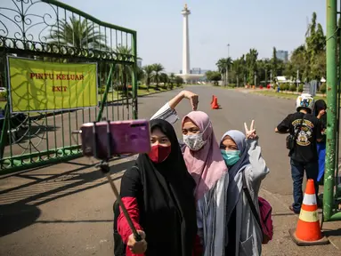 Sejumlah warga berswafoto di depan kawasan Monumen Nasional (Monas), Jakarta, Minggu (26/7/2020). Sejumlah warga mulai mengunjungi kawasan Monas meski masih ditutup sementara di masa PSBB transisi. (Liputan6.com/Faizal Fanani)