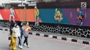 Mahasiswa melintas di depan mural bertema Asian Games 2018 di kawasan Universitas Negeri Jakarta, Kamis (16/8). Mural karya mahasiswa seni rupa tersebut dibuat dalam rangka menyambut Asian Games 2018. (Liputan6.com/Immanuel Antonius)