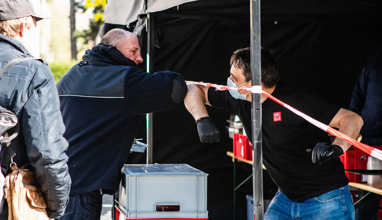 Seorang staf perusahaan katering (kiri) melakukan salam siku dengan seorang pria yang datang untuk mendapatkan makanan gratis di Berlin, ibu kota Jerman (16/4/2020). (Xinhua/Binh Truong)