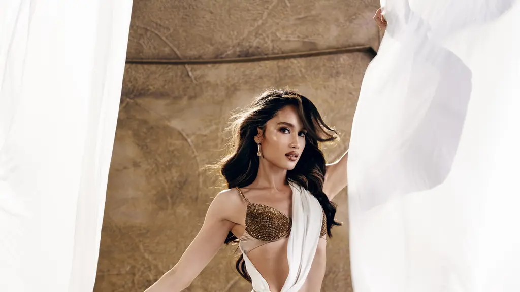 Cinta Laura tampil bak Dewi Athena dengan gaun putih berbahan chiffon yang dililitkan asimetris dan berpotongan cut-out di pinggang. Atasan berhias kristal emas serta bros bunga matahari dari batu kristal besar menjadi pusat perhatian, dipadukan sayap bulu emas yang megah dan heels gladiator emas bertali tinggi. [@claurakiehl]