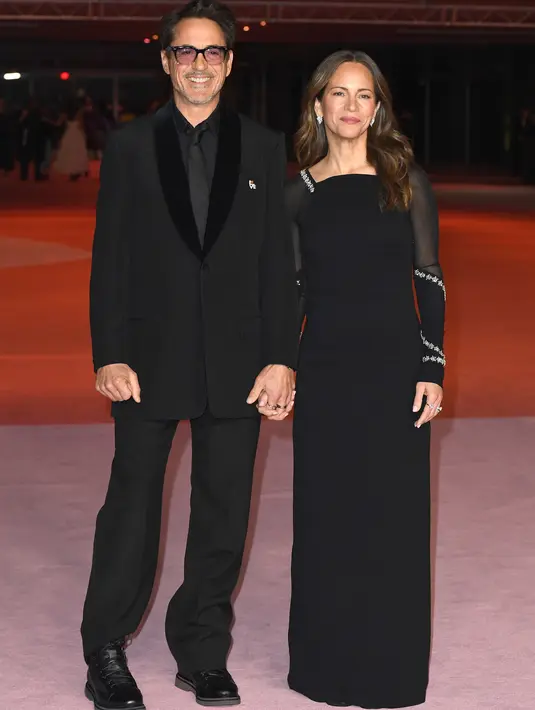 Robert Downey Jr. dan Susan Downey tampil mengenakan koleksi Givenchy Spring/Summer 2024. Robert Downey Jr. memilih mengenakan black wool jacket dengan velvet shawl lapel, dipadu mengenakan celana yang serasi, black cotton poplin shirt, dan black silk tie. Sedangkan Susan tampil mengenakan black silk crepe backless dress dengan crystal stars embroidery. [Foto: Document/Givenchy]