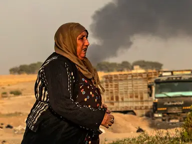 Seorang wanita berjalan saat asap mengepul menyusul pemboman Turki di Kota Ras al-Ain, Provinsi Hasakeh, Suriah, Rabu (9/10/2019). Turki mulai menggelar operasi militer untuk menyasar milisi Kurdi di utara Suriah. (Delil SOULEIMAN/AFP)