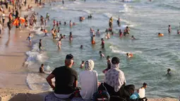 Warga Palestina mengamati pengnjung yang bermain air di pantai Beit Lahia di Jalur Gaza utara saat para siswa memulai liburan musim panas mereka pada 3 Juni 2022. Sejumlah warga menikmati musim panas dengan berenang dan bermain air di pantai. (MOHAMMED ABED / AFP)