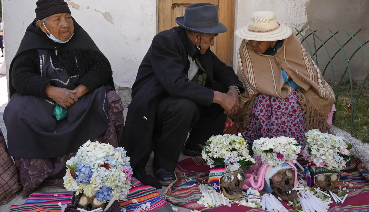 Orang-orang duduk dengan tengkorak manusia yang dihias untuk diberkati oleh seorang imam selama Festival Natitas di Pemakaman Umum di La Paz, Bolivia, Selasa (8/11/2022). Tradisi tahunan ini merayakan kematian di Bolivia dengan tengkorak yang dirawat dan didekorasi oleh mereka yang menggunakannya sebagai jimat untuk perlindungan. (AP Photo/Juan Karita)