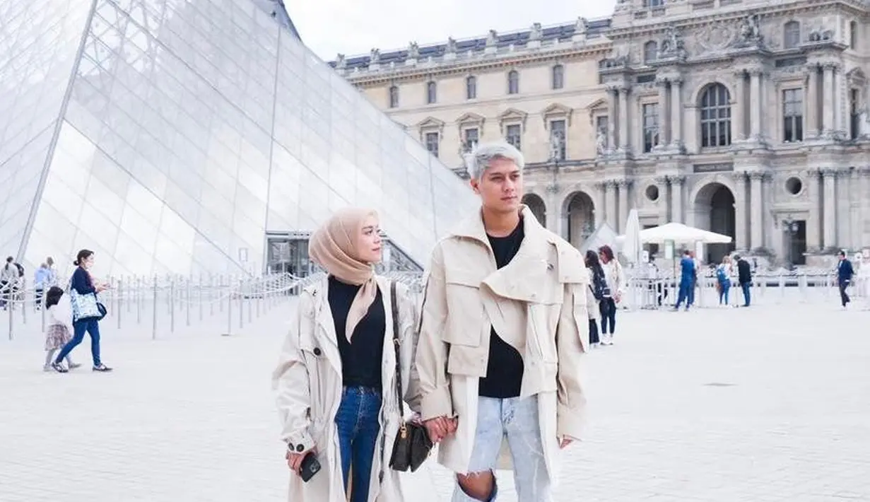 Berpose di Museum Louvre, keduanya kompak pakai trench coat dan kaos hitam. (Instagram/rizkybillar).