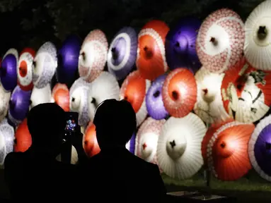Pengunjung mengambil foto lentera berbentuk payung tradisional yang dinyalakan untuk menandai peringatan 100 tahun Kuil Meiji Jingu Shinto di Tokyo, Jumat (30/10/2020). Meiji Jingu, dibangun untuk memberi penghormatan kepada Kaisar Meiji dan Permaisuri Shoken pada tahun 1920 (AP Photo/Eugene Hoshiko