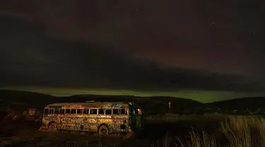 Sebuah aurora borealis, juga dikenal sebagai cahaya utara, terlihat di langit malam saat awan bergerak di atas tengara pinggir jalan yang dikenal sebagai "That NW Bus" di Washtucna, Washington, Amerika Serikat, 27 Februari 2023 dini hari. Berdenyut dalam garis-garis merah, hijau, dan ungu, aurora – juga dikenal sebagai cahaya utara – tampil semarak di belahan bumi utara dari Minggu malam hingga Senin pagi. (AP Photo/Ted S. Warren)