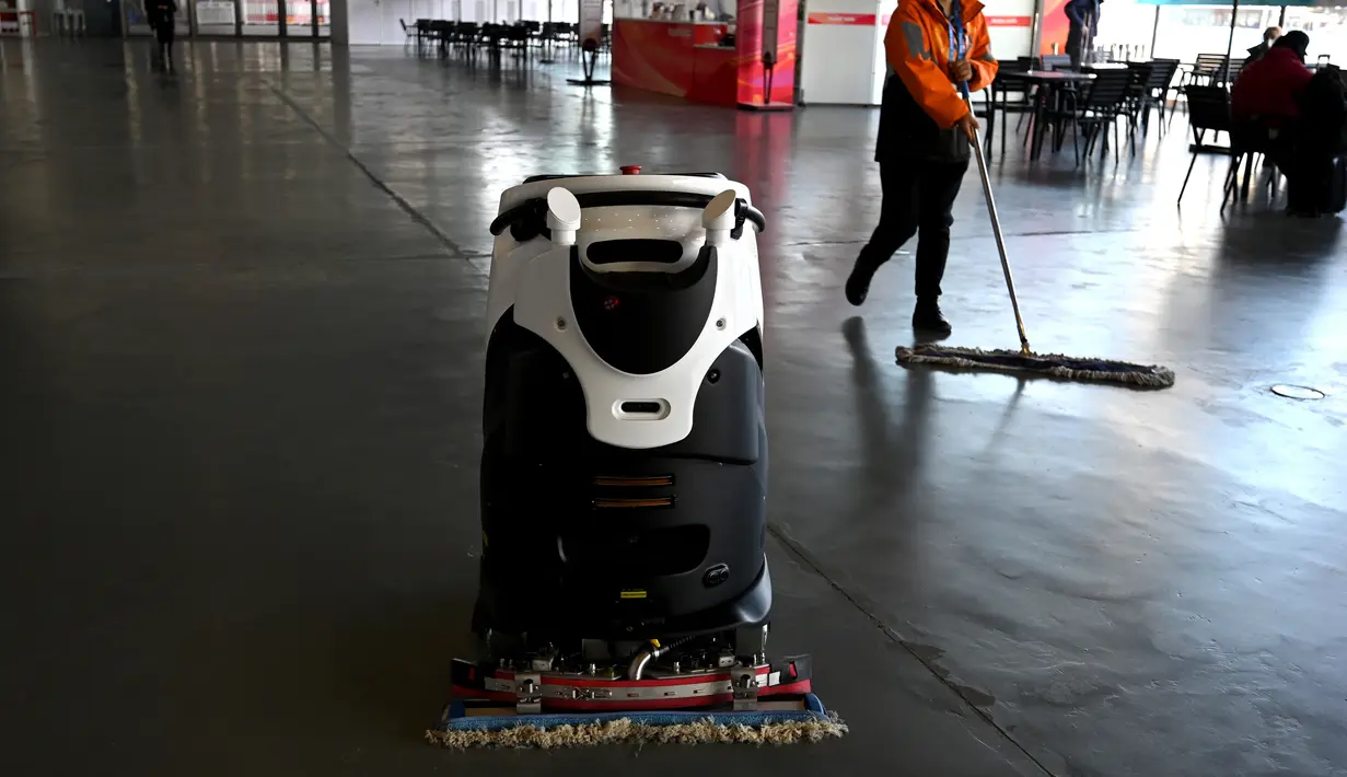 Robot dan seorang karyawan membersihkan lantai Pusat Media Utama selama Olimpiade Musim Dingin Beijing 2022 pada 5 Februari 2022. (AFP/Gabriel Bouys)