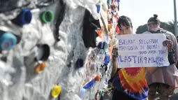 Peserta mengangkat poster dekat instalasi "monster plastik" dalam pawai bebas plastik di Taman Aspirasi Monas, Jakarta, Minggu (21/7/2019). Monster plastik berupa rangka berbentuk menyerupai ikan Angler Fish setinggi 4 meter tersebut dibuat dari 500 kg sampah plastik. (merdeka.com/Iqbal S Nugroho)