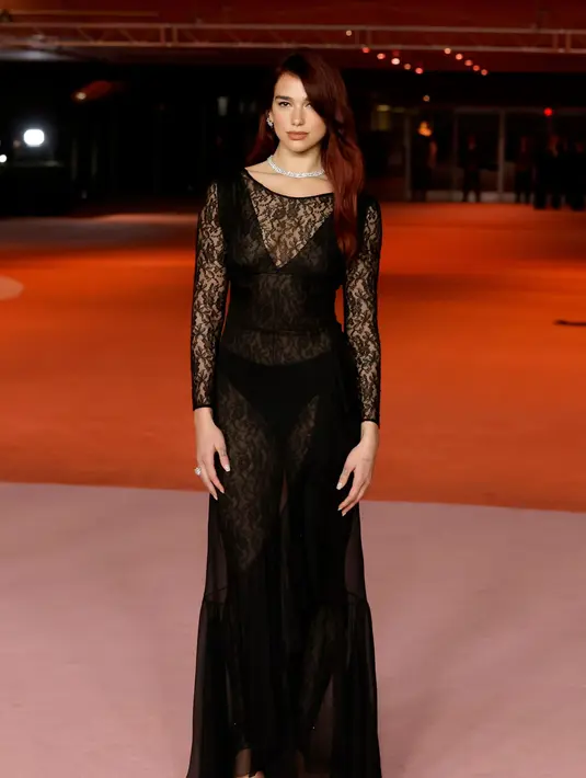 Dua Lipa mengenakan jumpsuit renda hitam ditumpuknya dengan gaun muslin hitam. Penampilannya ini berasal dari koleksi Chanel Métiers d’art 2020. [Foto: Document/Chanel]