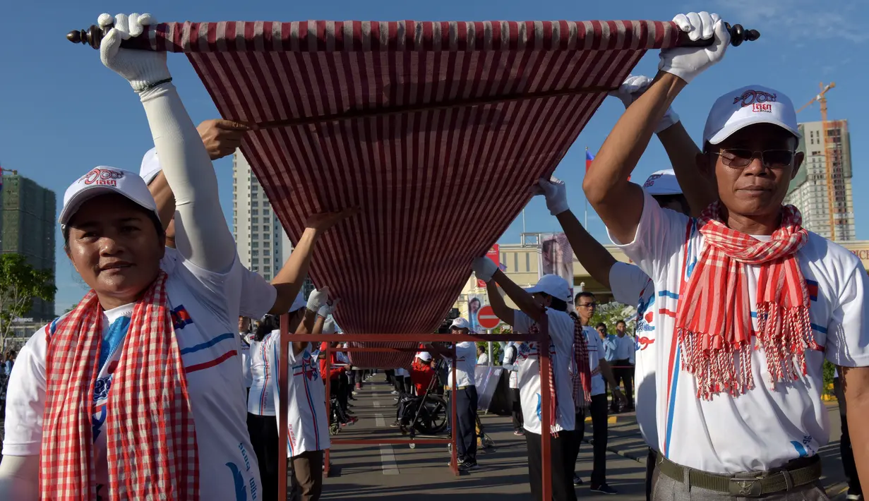 Warga Kamboja membentangkan syal krama untuk memecahkan rekor Guinness sebagai syal tenun terpanjang dunia di Phnom Penh, Minggu (1/7). Syal dengan panjang 1.149,8 meter dan lebar 88 cm tersebut dibentangkan di luar Istana Kerajaan. (AFP/TANG CHHIN Sothy)
