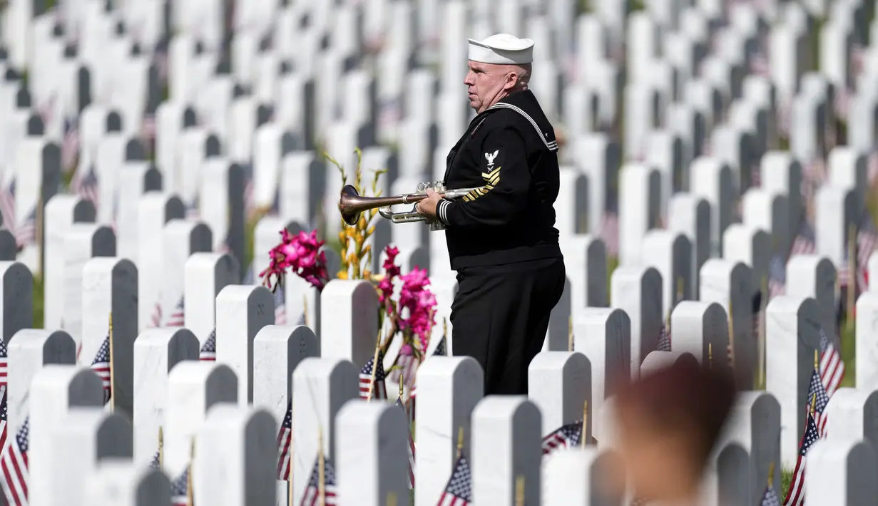Pensiunan Angkatan Laut Amerika Serikat Yeoman Mark Stallins berjalan melewati deretan batu nisan saat akan memainkan Taps untuk keluarga prajurit yang gugur di sebuah kuburan di Pemakaman Nasional Fort Logan, Sheridan, Colorado, Amerika Serikat, 30 Mei 2022. (AP Photo/David Zalubowski)