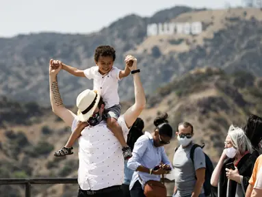 Pengunjung mengenakan masker di luar ruangan saat mengambil gambar tanda Hollywood di Observatorium Griffith di Los Angeles, Senin (17/5/2021). California mempertahankan aturan mengenakan masker hingga negara bagian itu mencabut pembatasan COVID-19 pada 15 Juni. (AP Photo/Damian Dovarganes)