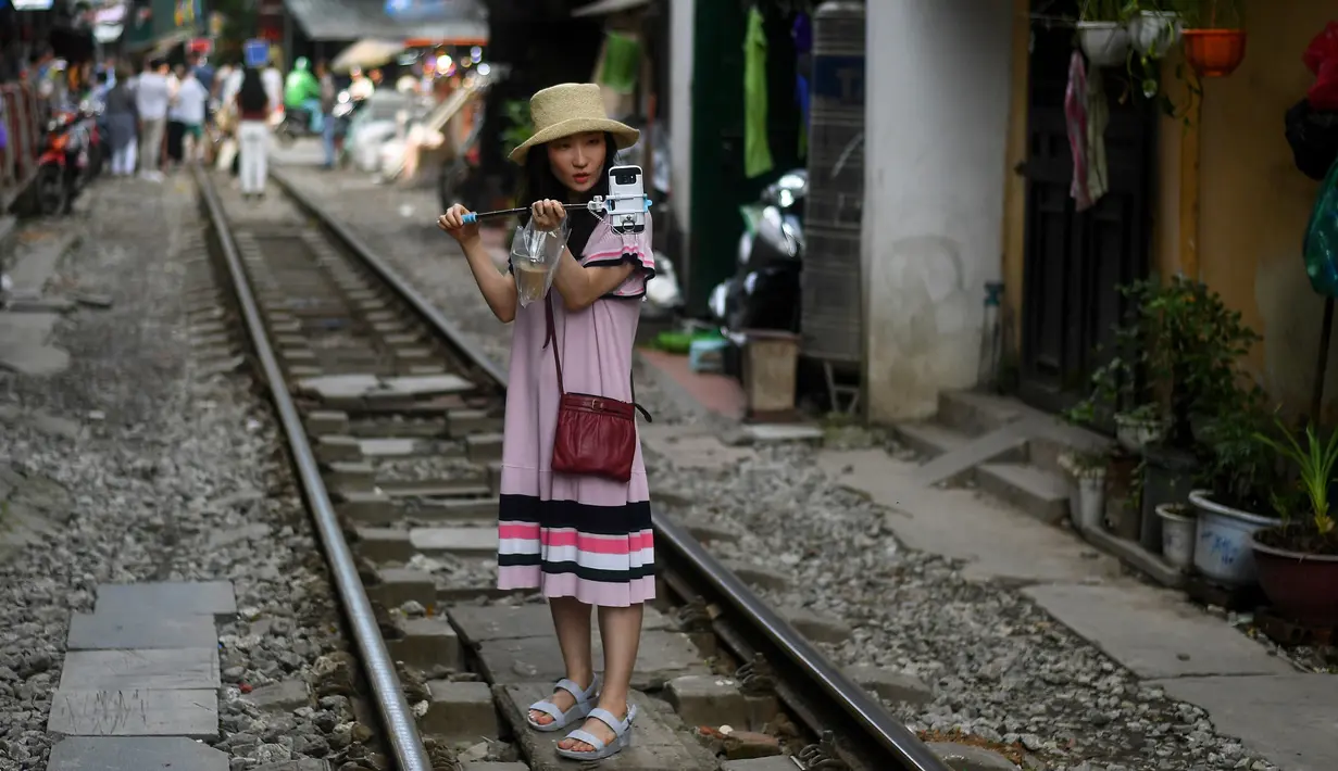Foto pada 8 Juni 2019 memperlihatkan seorang wanita berswafoto di tengah jalur kereta api populer di Hanoi, Vietnam. Turis sengaja datang ke Old Quarter untuk berfoto di rel kereta api yang dianggap ' instagramable' tersebut. (Photo by Manan VATSYAYANA / AFP)