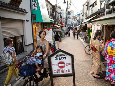 Seorang wanita mengendarai sepeda membawa anak-anaknya melihat ke arah sejumlah wanita yang mengenakan pakaian tradisional yang berbelanja di jalan Yanaka ginza di pusat Tokyo (30/9/2019). Wilayah Yanaka di ibukota Jepang dikenal sebagai salah satu yang paling kuno dan unik. (AFP Photo/Odd Andersen)