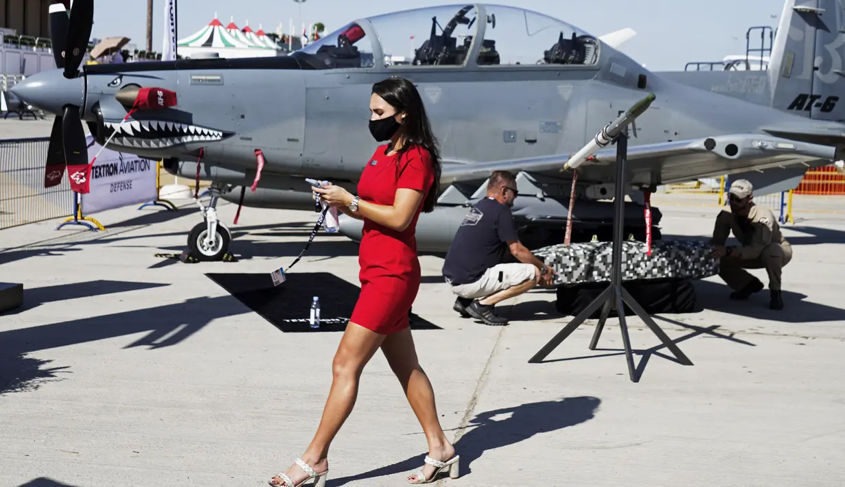Seorang wanita berjalan melewati pesawat serang ringan Beechcraft AT-6 Wolverine saat kru memasang perangkat di sayapnya di Dubai Air Show di Dubai, Uni Emirat Arab (14/11/2021). (AP Photo/Jon Gambrell)