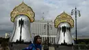 Seorang gadis bermain di depan "benda seni Matryoshki", tujuh boneka bersarang tradisional Rusia "matryoshka" bercermin di atasnya dengan hiasan kepala "kokoshnik", dengan gedung Pemerintah Rusia terlihat di latar belakang, di pusat kota Moskow (9/9/2021).  (AFP/Kirill Kudryavtsev)