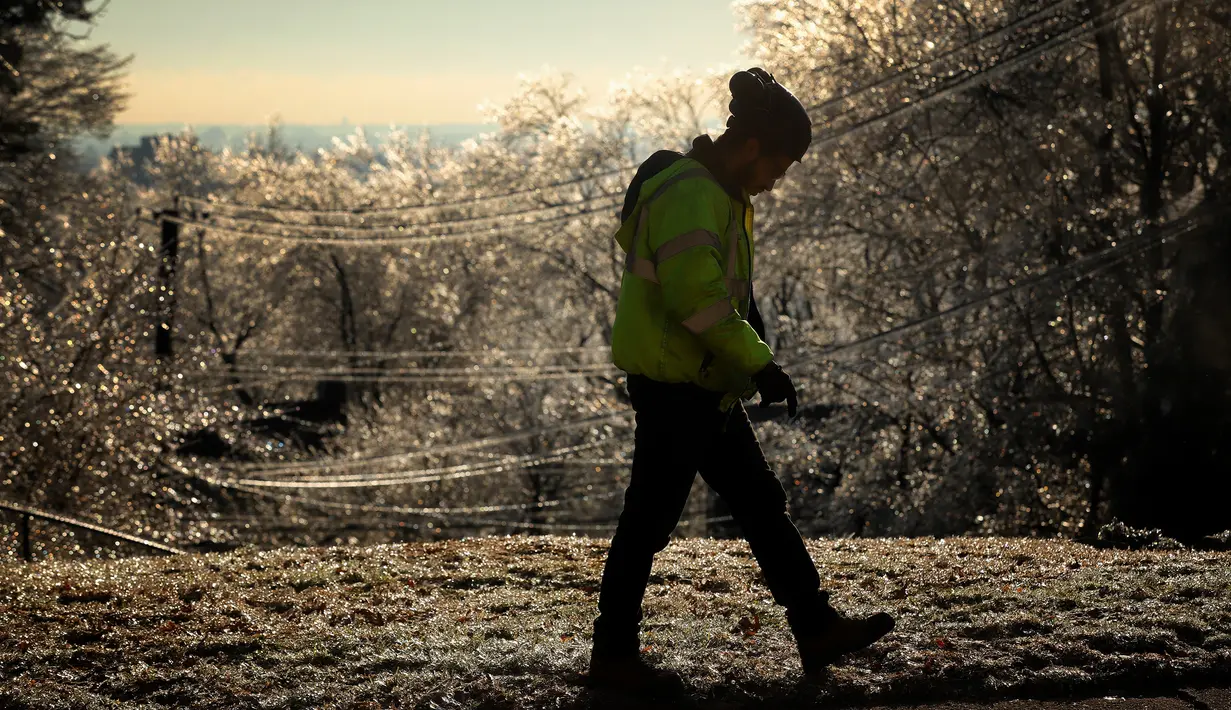 Seorang pekerja berjalan di sisi jalan ketika pohon-pohon membeku saat badai musim dingin di West Orange, New Jersey (18/12/2019). Suhu dingin tersebut diharapkan turun pada Kamis pagi. (Rick Loomis/Getty Images/AFP)