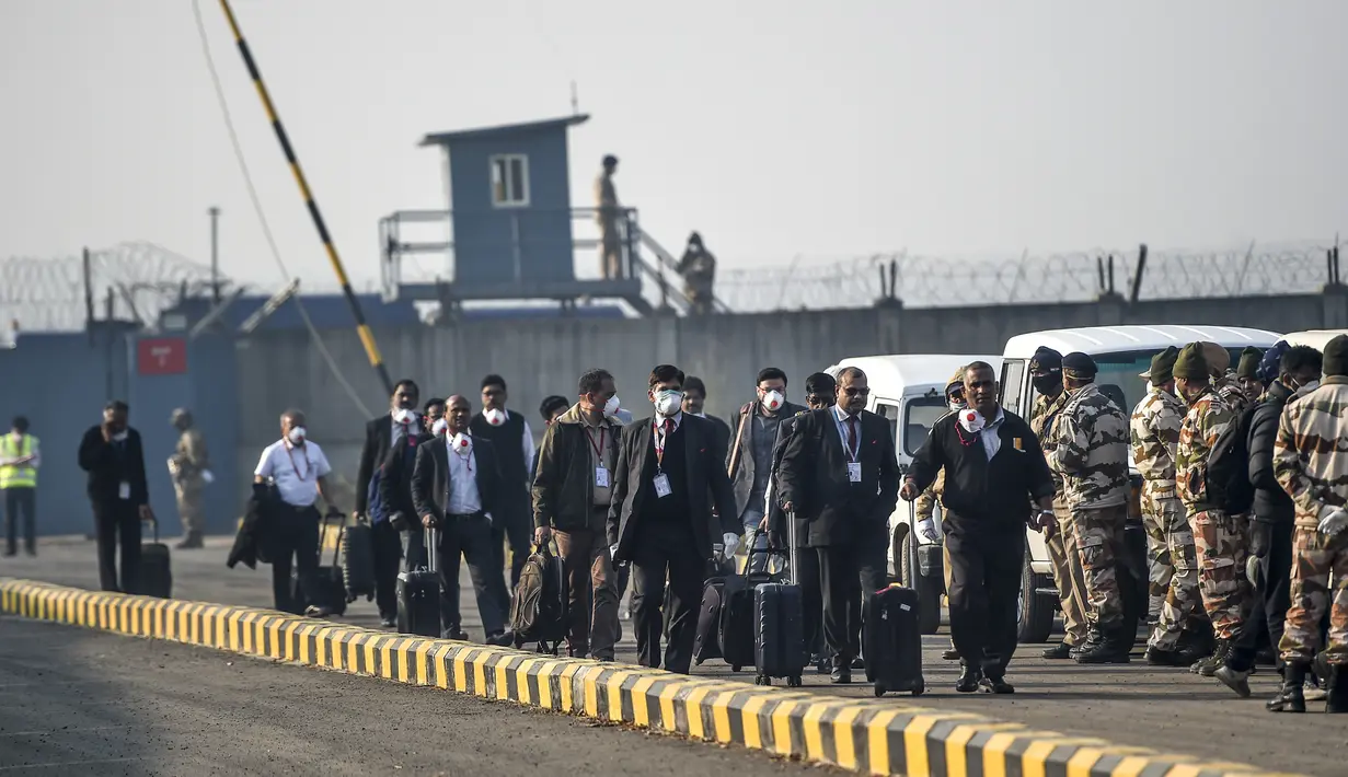 Anggota kru dan pejabat mengenakan masker membawa barang-barang mereka di Bandara Internasional Indira Gandhi setelah evakuasi warga negara India dari kota Wuhan, Cina, di New Delhi (1/2/2020). (AFP/Money Sharma)