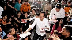 Presiden Joko Widodo atau Jokowi bersama Gubernur NTB Tuan Guru Bajang (TGB) Zainul Majdi membagikan buku saat mengunjungi korban gempa di lapangan Desa Madayin, Sambelia, Lombok Timur, NTB, Senin (30/7). (Agus Suparto/Indonesian Presidential Palace/AFP)