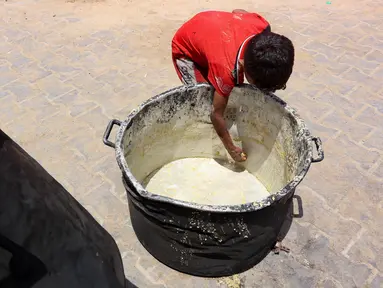 Seorang anak laki-laki Palestina mengorek sisa-sisa sup kacang miju-miju yang tersisa di dalam panci, di depan titik distribusi makanan di kamp pengungsian dekat pelabuhan Kota Gaza pada 22 Mei 2025. (Omar AL-QATTAA/AFP)