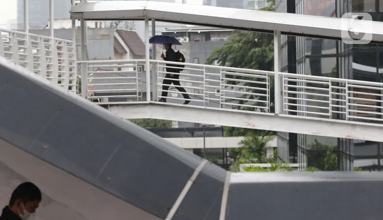 Warga menggunakan payung di Jembatan Penyebrangan Orang, kawasan Kuningan, Jakarta, Kamis (18/12/2021). BMKG memprakirakan potensi hujan lebat yang mungkin disertai petir dan angin kencang hingga 21 Februari di beberapa provinsi di Indonesia, termasuk DKI Jakarta. (Liputan6.com/Helmi Fithriansyah)