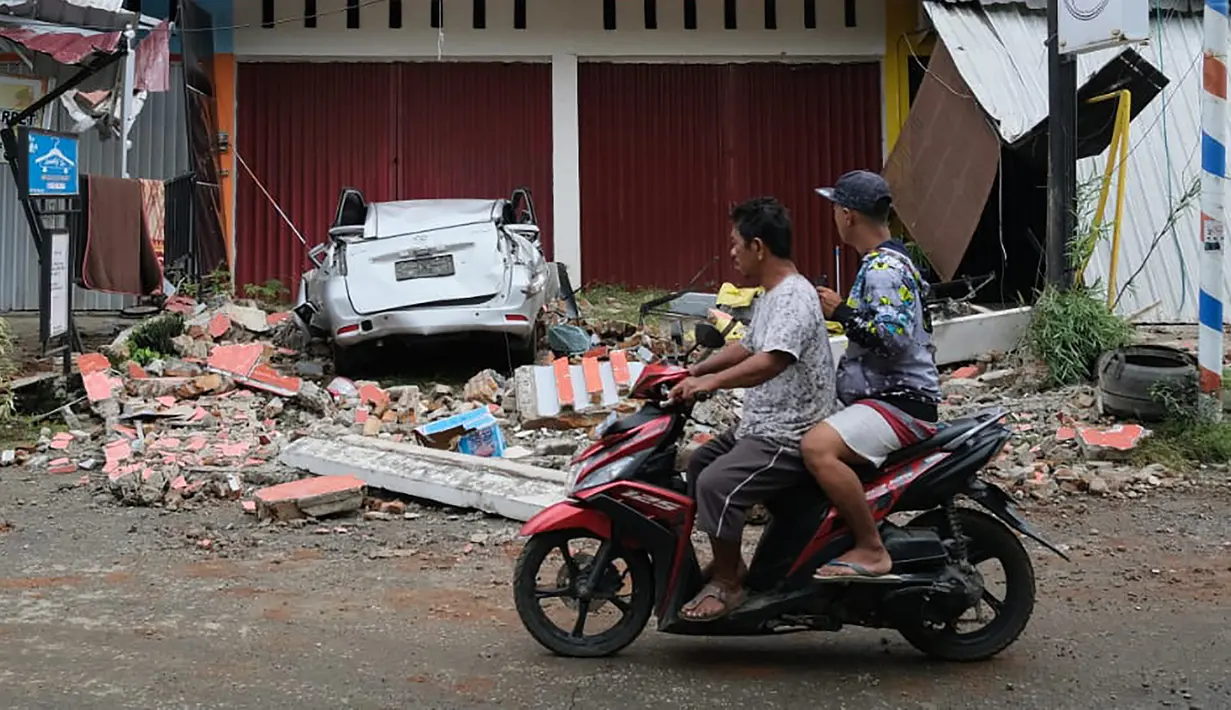 Pengendara motor melihat sebuah mobil yang hancur akibat gempa bumi di Mamuju, Sulawesi Barat,  Jumat (15/1/2021). Jaringan listrik di wilayah itu juga dilaporkan mengalami pemadaman. (AP Photo/Sadly Ashari Said)