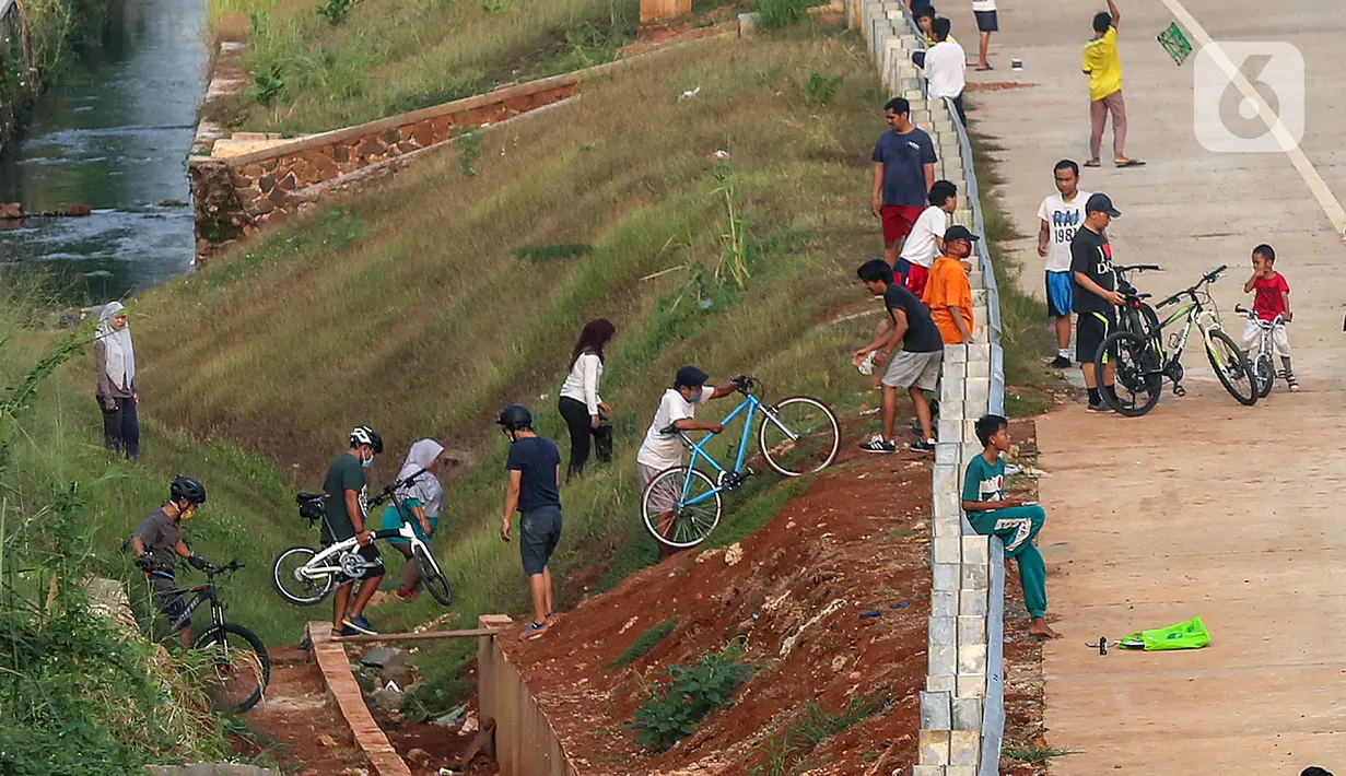 Warga menyeberangi selokan untuk bersepeda di kawasan Tol Serpong Kunciran, Ciputat, Tangerang Selatan, Kamis (25/6/2020). Selama PSBB Tangerang Raya, warga memanfaatkan waktu untuk berolahraga dan bermain layang-layang sambil hingga menjelang matahari terbenam. (Liputan6.com/Fery Pradolo)