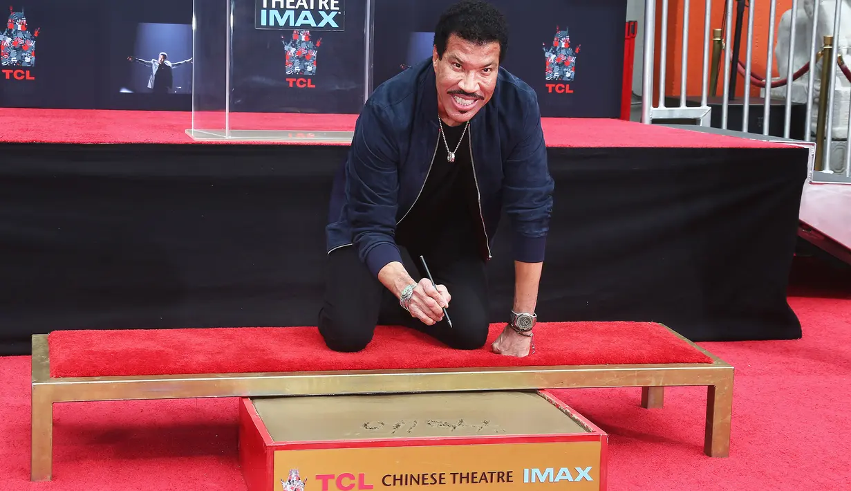 Lionel Richie membubuhkan tanda tangan sebelum mengabadikan cetak tangan dan kakinya di TCL Chinese Theatre, Hollywood, Rabu (7/3). Richie menerima berbagai penghargaan internasional dan penghargaan dari sejumlah negara. (Tommaso Boddi/Getty Images/AFP)