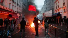 Seorang anggota komunitas Kurdi mengibarkan bendera komunis Kurdi dekat barikade yang terbakar di TKP tempat terjadinya penembakan di Paris, Prancis, 23 Desember 2022. Demonstrasi memprotes penembakan komunitas suku Kurdi di Paris berujung rusuh. (AP Photo/Lewis Joly)
