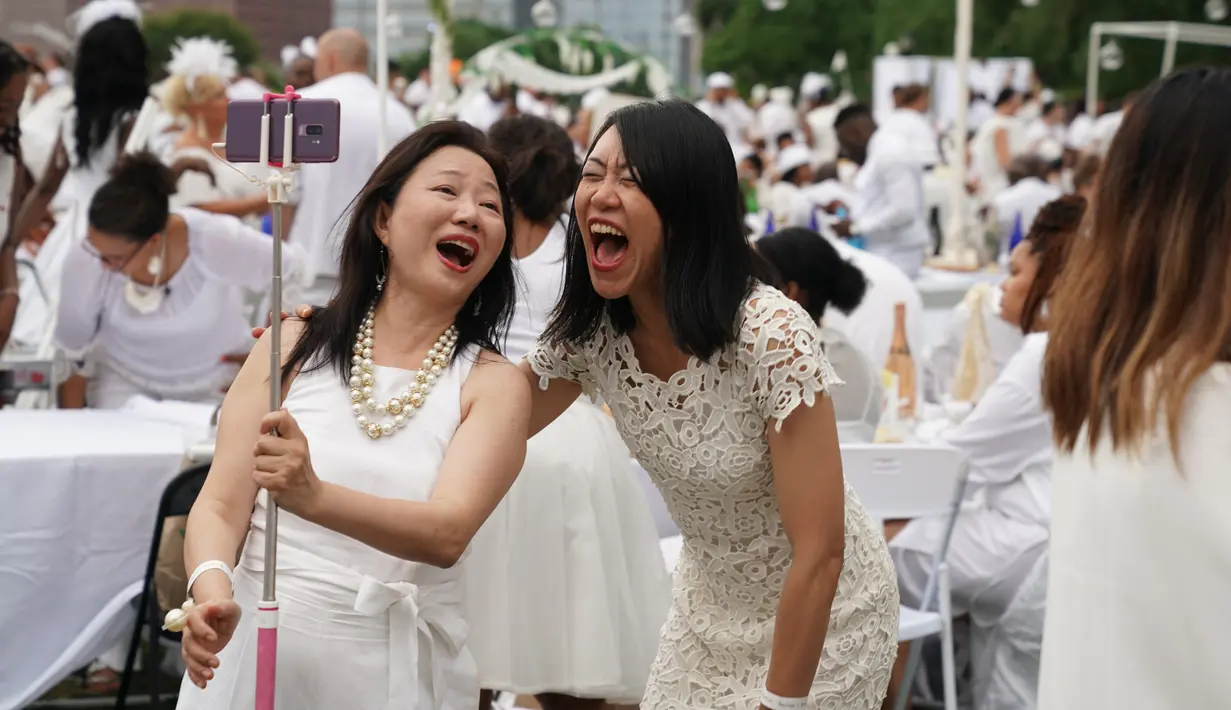 Dua wanita berpakaian serba putih bersuka ria dalam Diner en blanc di Rockefeller Park, New York, Rabu (17/7/2019). New York City Diner en Blanc adalah sebuah pesta makan malam rahasia dengan pakaian bernuansa putih yang diadopsi dari budaya Prancis. (TIMOTHY A. CLARY / AFP)