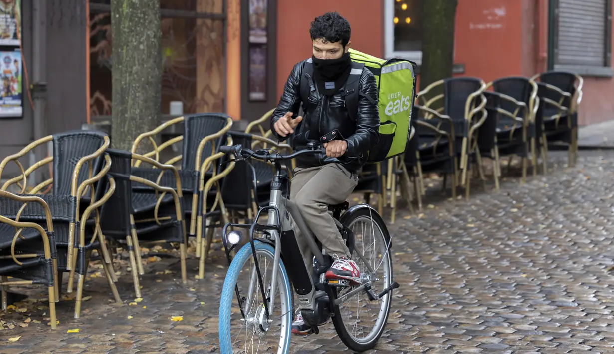 Seorang pengantar makanan Uber memakai masker saat melewati teras kosong di kawasan Marrolles di Brussels, Rabu (17/11/2021). Pemerintah Belgia mewajibkan kembali penggunaan masker dan memberlakukan warga bekerja dari rumah dalam upaya menahan lonjakan baru kasus COVID-19. (AP Photo/Olivier Matthys)