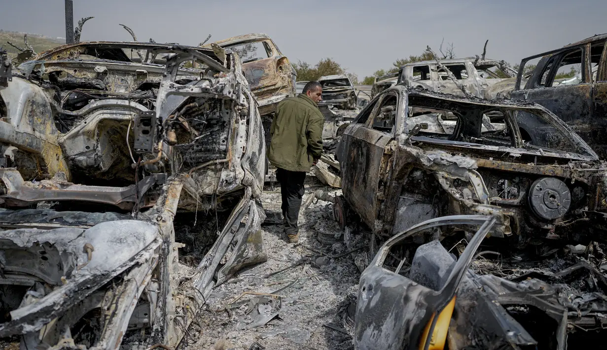 Seorang pria Palestina berjalan di antara mobil-mobil yang hangus di tempat pembuangan sampah, di kota Hawara, dekat kota Nablus di Tepi Barat, Senin, 27 Februari 2023. Puluhan pemukim Israel mengamuk dengan kekerasan di Tepi Barat utara, membakar  mobil dan rumah-rumah setelah dua pemukim dibunuh oleh seorang pria bersenjata Palestina. (AP Photo/Ohad Zwigenberg)