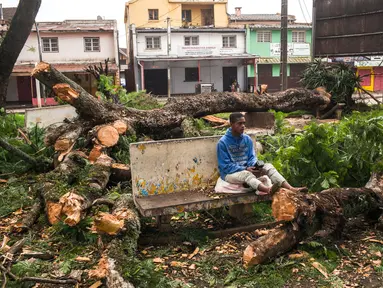 Seorang pria duduk di bangku di tengah pohon yang tumbang dan jatuh di taman umum di pusat Antsirabe setelah berlalunya topan Batsirai pada 6 Februari 2022. Sedikitnya enam orang dan membuat hampir 48.000 orang mengungsi ketika Topan Batsirai melanda Madagaskar. (RIJASOLO/AFP)