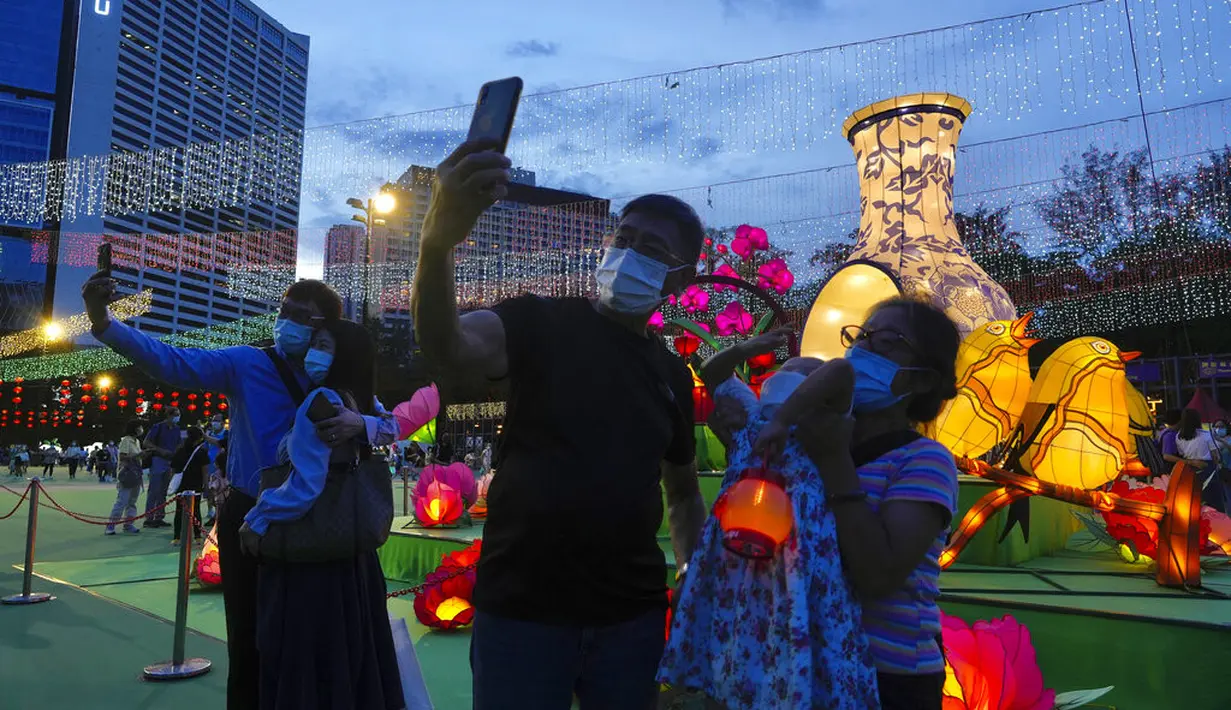 Orang-orang berswafoto di depan lentera yang menyala selama Festival Pertengahan Musim Gugur di taman Victoria di Hong Kong, Selasa (21/9/2021).  Festival ini didatangi keluarga dan teman Tionghoa untuk berkumpul makan kue bulan China dan pomelo bersama-sama. (AP Photo/Vincent Yu)