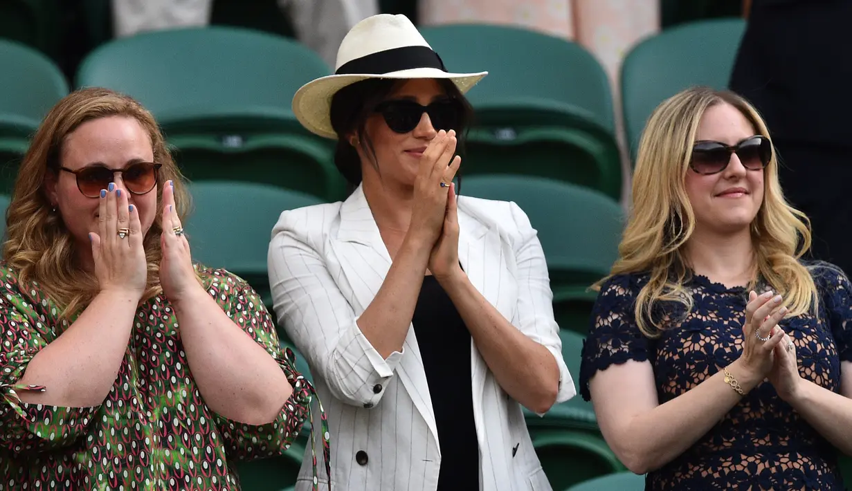 Meghan Markle (tengah) bertepuk tangan usai petenis AS Serena Williams menang atas Kaja Juvan dari Slovakia pada babak kedua Wimbledon di All England Lawn Tennis Club, London, Kamis (4/7/2019). Meghan menyambangi lapangan tenis Wimbledon ditemani dua sahabat semasa di kampusnya dulu. (GLYN KIRK/AFP)