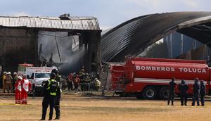 Petugas pemadam kebakaran dan pekerja Palang Merah menangani lokasi jatuhnya sebuah pesawat di dekat Bandara Toluca, di San Mateo Atenco, Meksiko, pada hari Senin (15/12/2025). (Dok. AP/Ramses Mercado)