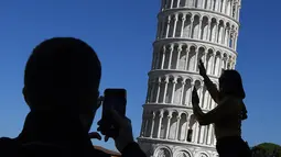 Turis berpose di depan Menara Pisa di kota Pisa, Italia pada 28 November 2018. Setelah upaya yang dilakukan selama lebih dari dua puluh tahun, para insinyur mengatakan kemiringan menara setinggi 57 meter itu telah berkurang 4 cm. (Tiziana FABI / AFP)