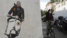 Seorang wanita mengendarai sepedanya di dekat mural Jose Mourinho mengendarai skuter Vespa mengenakan syal merah dan kuning berhias lambang AS Roma di lingkungan Testaccio, Roma (7/5/2021). Mourinho resmi menjabat sebagai pelatih AS Roma untuk musim depan. (AP Photo/Gregorio Borgia)