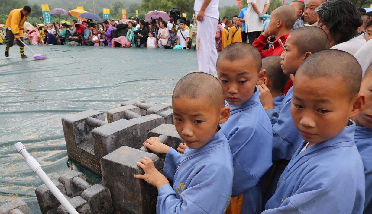 Biksu muda Shaolin berdiri di samping kunci batu saat menyaksikan kompetisi seni bela diri '72 Arts of Shaolin' di kuil Shaolin, Provinsi Henan, China, 30 Juli 2017. Kompetisi ini menampilkan para jago kungfu yang memamerkan kekuatan fisik. (STR AFP)