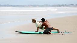 Seorang pendamping memberikan pelatihan dasar berselancar untuk para wisatawan atau pemula di Pantai Seminyak, Bali. (Bola.com/M iqbal Ichsan)