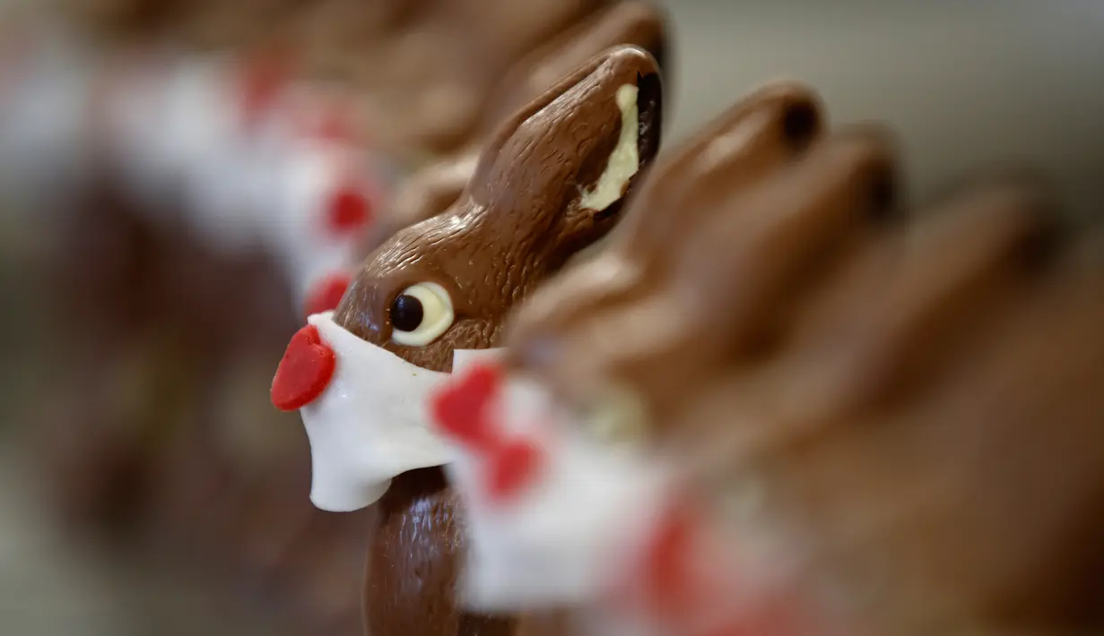 Pekerja menyiapkan cokelat paskah berbentuk kelinci yang mengenakan masker di toko roti Baeckerei Bohnenblust di Bern, Swiss, Jumat (27/3/2020). Cokelat paskah yang dibuat di tengah pandemi virus corona yang sedang merebak di seluruh dunia ini dijual sekitar RP 143 ribu. (STEFAN WERMUTH/AFP)