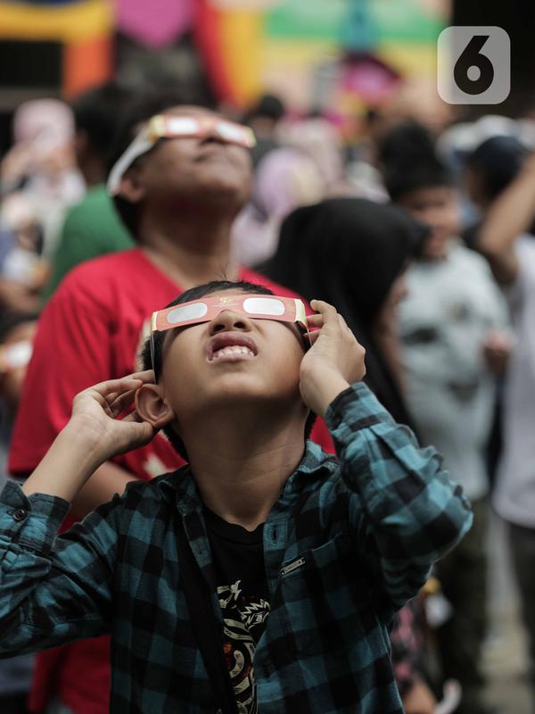 Pengunjung mengamati gerhana matahari cincin memakai kacamata khusus di Planetarium Taman Ismail Marzuki, Jakarta, Kamis (26/12/2019). Planetarium menyediakan sekitar 10 teleskop dan kacamata khusus agar pengunjung bisa menyaksikan gerhana matahari cincin dengan aman. (Liputan6.com/Faizal Fanani)