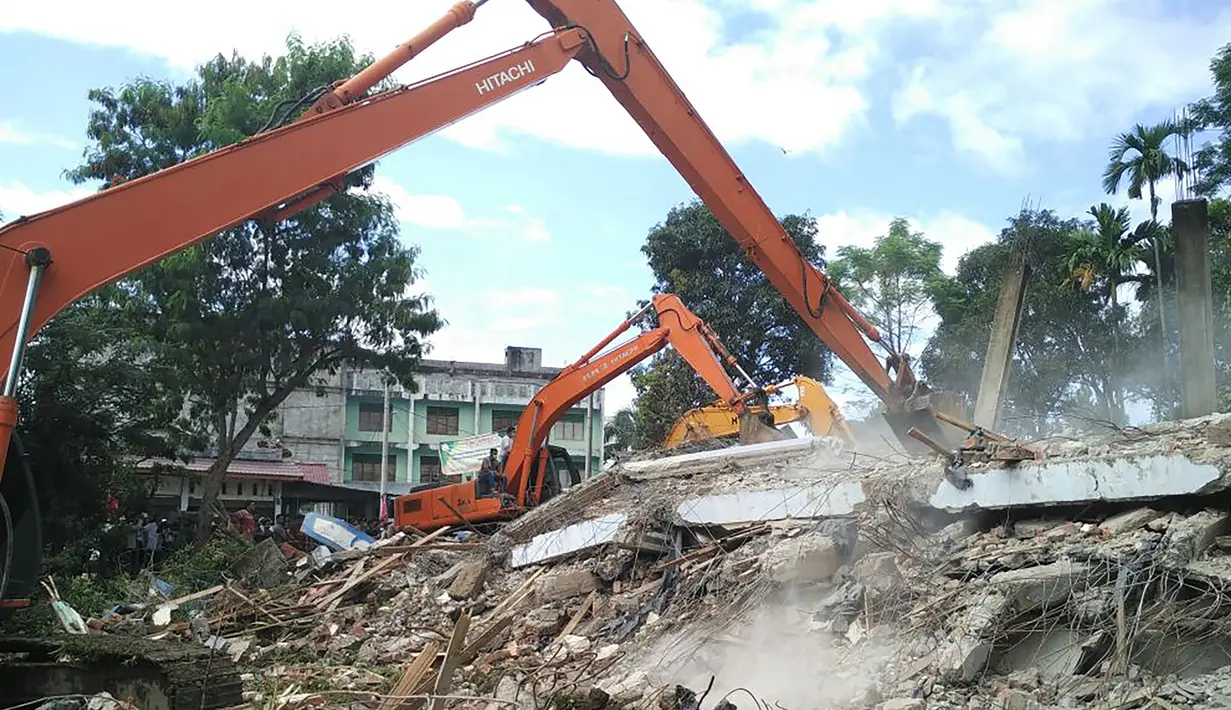 Petugas di bantu alat berat saat mengevakuasi korban gempa 6,4 SR di Kabupaten Pidie Jaya, Aceh, Rabu (7/12). Data BPBD juga mencatat ada 65 korban luka yang dirawat di RSUD Pidie Jaya akibat gempa Aceh. (AFP PHOTO/Chaideer Mahyuddin)