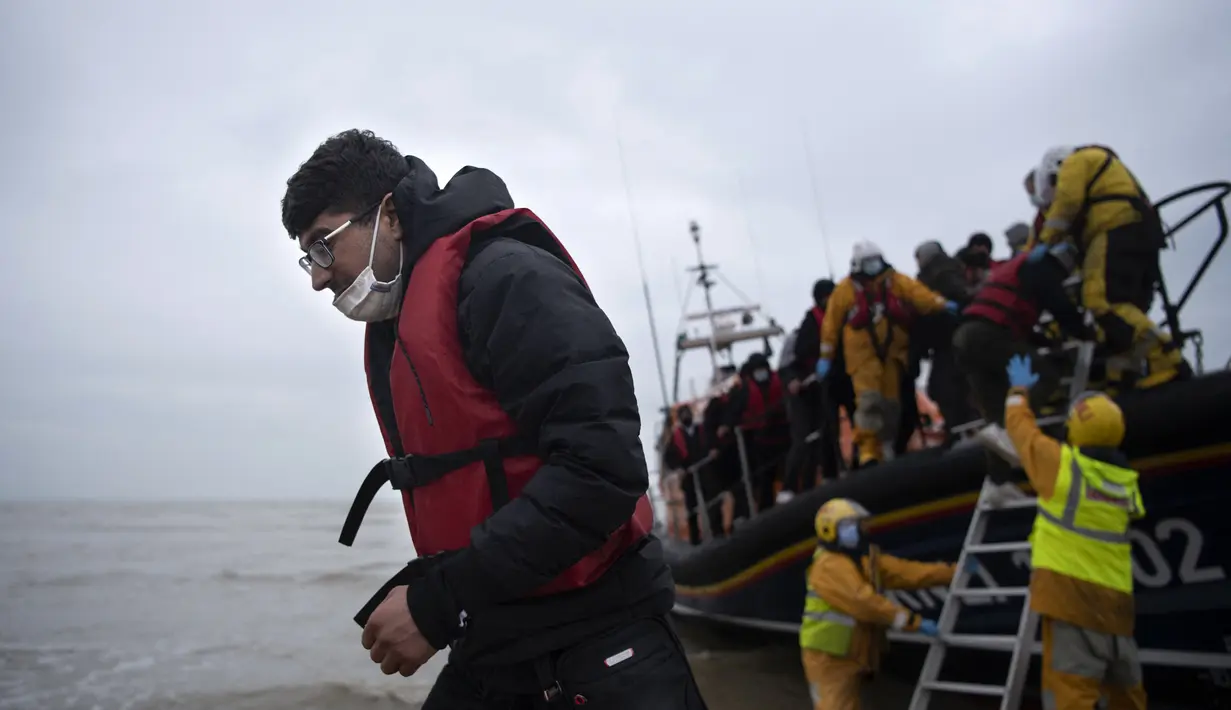 Para migran dibantu ke darat dari sekoci RNLI (Royal National Lifeboat Institution) setelah diselamatkan saat melintasi Selat Inggris di sebuah pantai di Dungeness, Inggris tenggara (24/11/2021). (AFP/Ben Stansall)